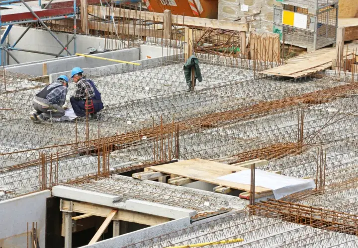 Bauarbeiter prüfen Pläne für verschiedene betondecken arten. Stahlbewehrung für eine massive Betonplatte ist sichtbar.