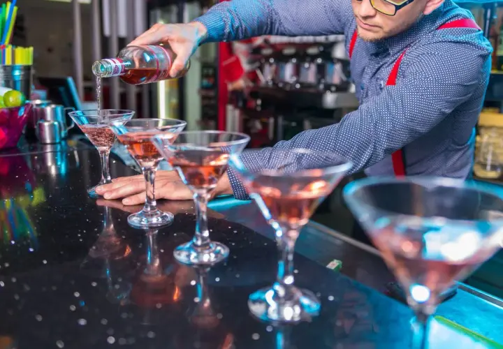 Barman nalewa różowy drink do kieliszków na barze.