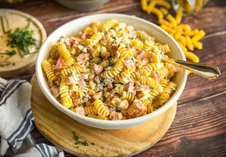 Herzhafter Nudelsalat mit Fleischsalat, Erbsen und einer cremigen Sauce, garniert mit frischen Kräutern.