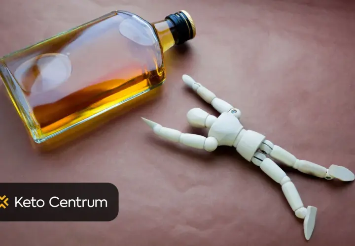Drewniany ludzik leży obok butelki alkoholu, symbolizując negatywny wpływ alkoholu na testosteron.