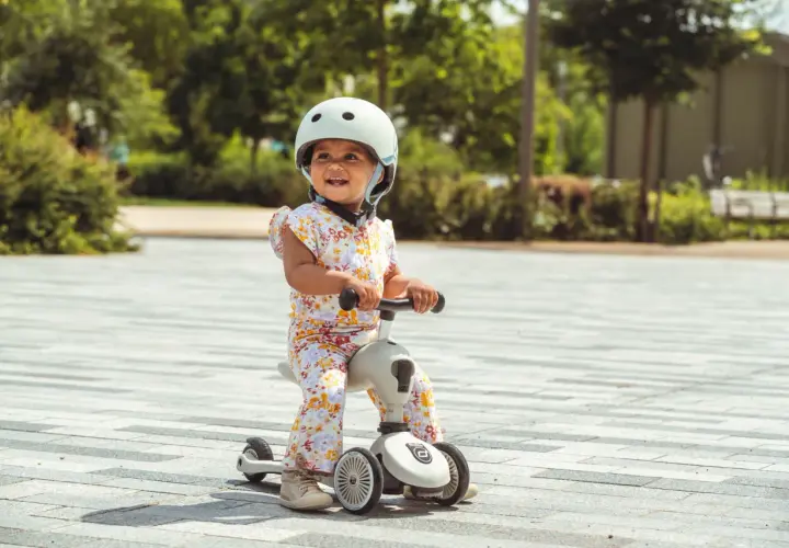 Uśmiechnięte dziecko w kasku na jeździku Scoot and Ride od kiedy zaczęło swoją przygodę z jazdą.