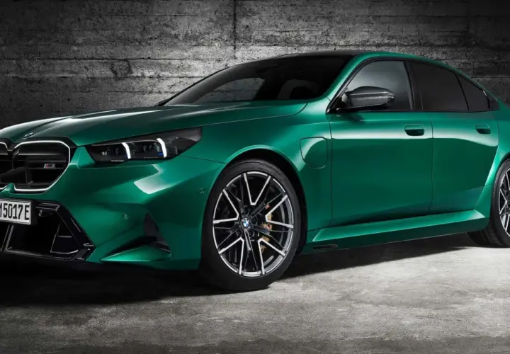 Zielony BMW M5 Competition z nowoczesnymi światłami i felgami stoi na tle betonowej ściany.