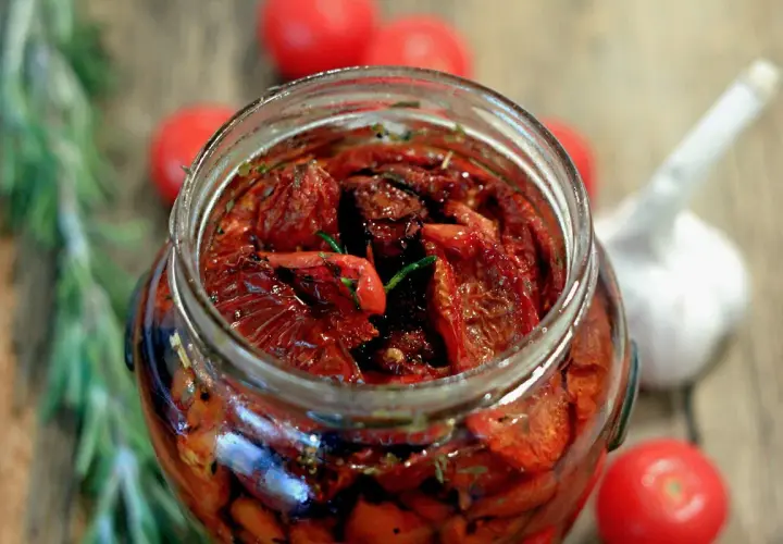 Pomodori secchi sott'olio, la ricetta della nonna. Un barattolo pieno di sapore, con rosmarino e aglio sullo sfondo.