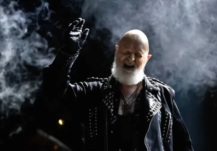 Rob Halford z Judas Priest, w skórzanej kurtce z ćwiekami, wznosi rękę w geście, jakby wykrzykując "Panic Attack" na koncercie.