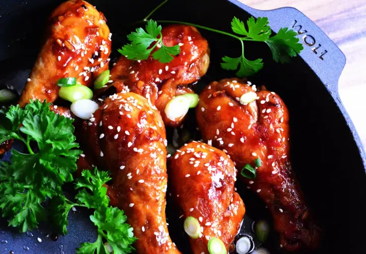 Kurczak teriyaki w glazurze z sezamem i szczypiorkiem w czarnej patelni.