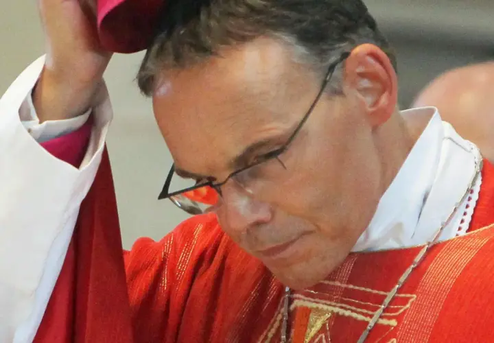 Bischof Tebartz van Elst trägt eine rote Messrobe und eine weiße Halskrause. Er blickt nach unten, während er eine Kopfbedeckung aufsetzt.