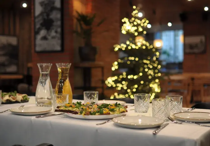 Stół wigilijny z przystawkami, napojami i ozdobioną choinką w tle. Zamówienia na wigilię w restauracji.