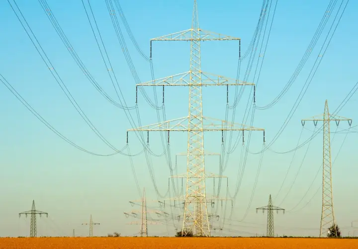 Linie energetyczne na tle błękitnego nieba. Wiele słupów wysokiego napięcia, tworzących sieć, jakby ilustrowało przelicznik MW na KW.
