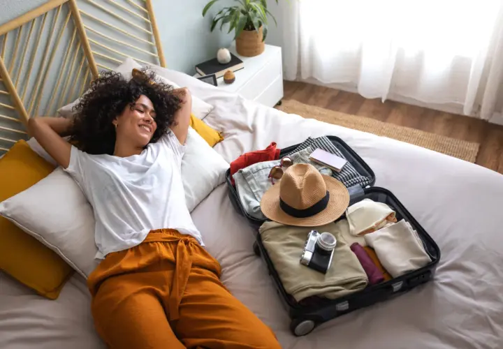 Une jeune femme se détend sur un lit, une valise ouverte à côté d'elle, prête pour son voyage. Elle est le parfait médiateur du tourisme, rêvant de nouvelles aventures.