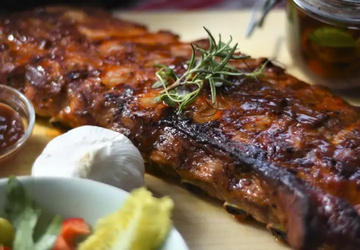 Soczyste żeberka w piekarniku, idealne do marynaty. Obok sos BBQ, czosnek i świeże zioła.