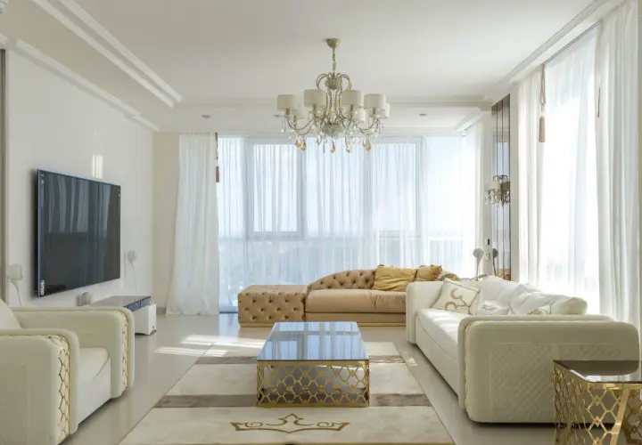 Elegancki salon w stylu nowojorskim, z jasnymi sofami, złotymi akcentami i kryształowym żyrandolem.
