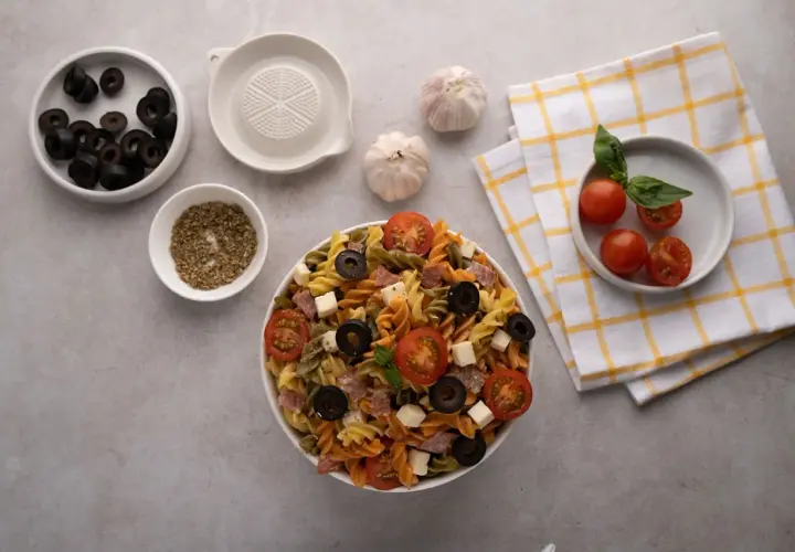 Deliciosa ensalada de pasta italiana con tomates, aceitunas, queso y salami. Ingredientes frescos listos para servir.