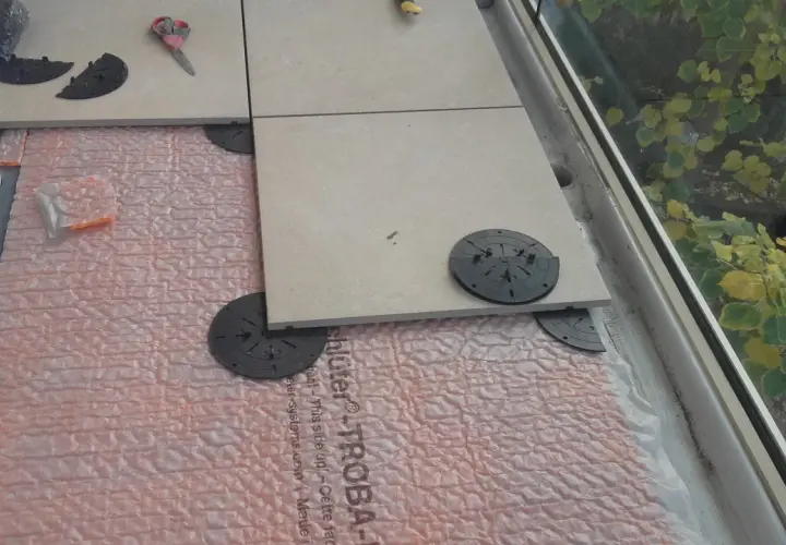 Installazione di un pavimento galleggiante su guaina bituminosa, con piastrelle in fase di posa su supporti regolabili.