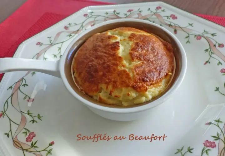 Un délicieux soufflé au beaufort, doré et gonflé, servi dans un ramequin sur une assiette décorée de rubans et de fleurs.