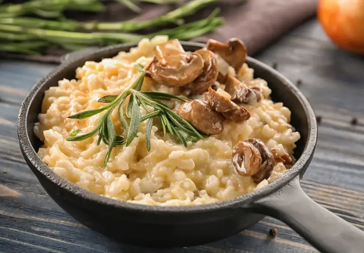 Cremoso arroz italiano con champiñones y romero, servido en sartén de hierro fundido.