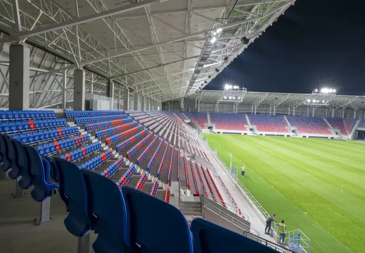 Puste trybuny stadionu Odra Opole w kolorach niebieskim i czerwonym, oświetlone nocą.