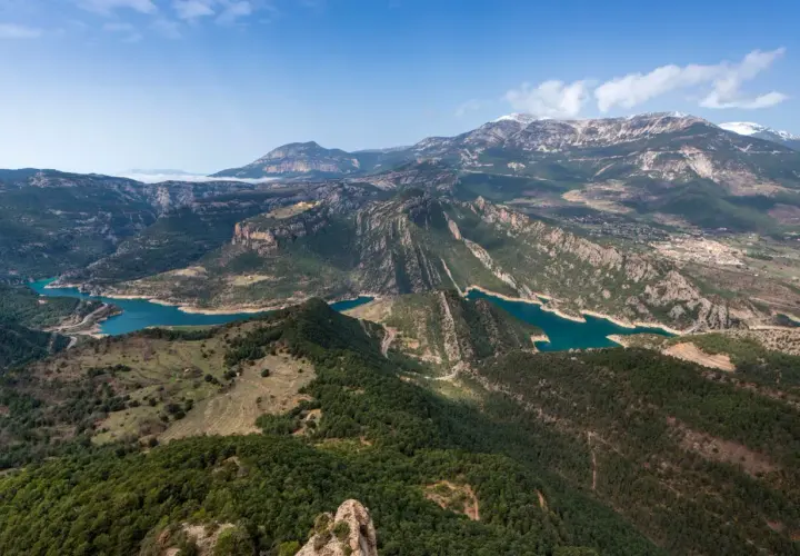 Paisaje montañoso con embalses de agua turquesa, ideal para explorar rutas Pirineos. Bosques verdes cubren las laderas y picos nevados al fondo.