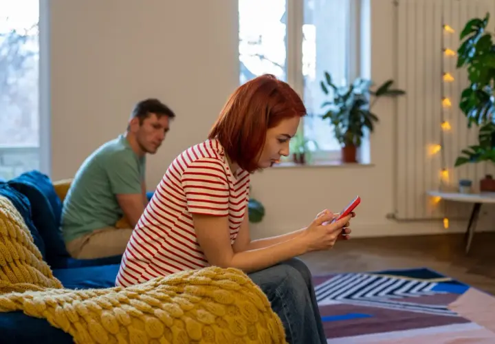 Ciężka atmosfera w domu, kiedy partner obwinia o wszystko. Ona ucieka w telefon, on patrzy z wyrzutem.