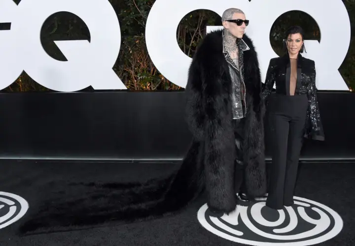 Travis Barker i jego żona Kourtney Kardashian na ściance GQ. Travis w ekstrawaganckim futrze, Kourtney w eleganckim garniturze.