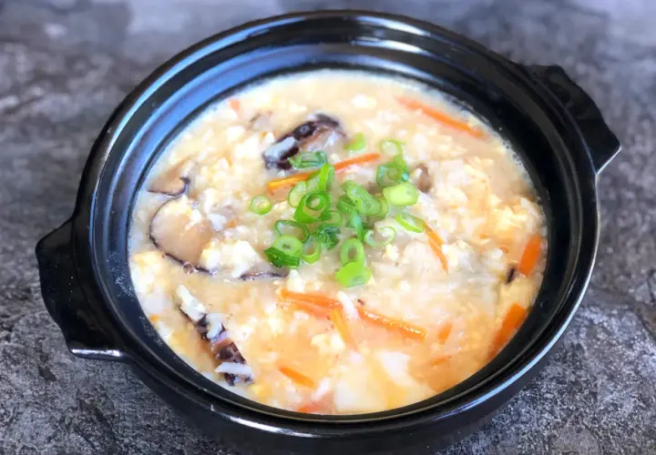 A comforting bowl of Japanese rice soup, also known as okayu, filled with tender rice, shiitake mushrooms, shredded carrots, and scrambled egg, garnished with fresh green onions.