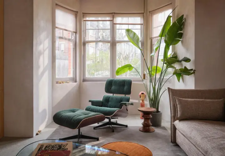 Gemütlicher mid century modern living room mit dunkelgrünem Sessel und Hocker, großem Fenster und einer Strelitzie.