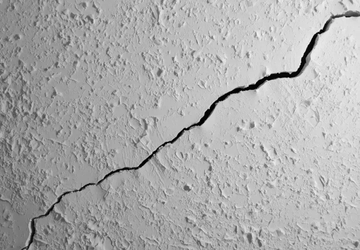 Une fissure traverse le plafond texturé d'un appartement, révélant une ombre profonde.