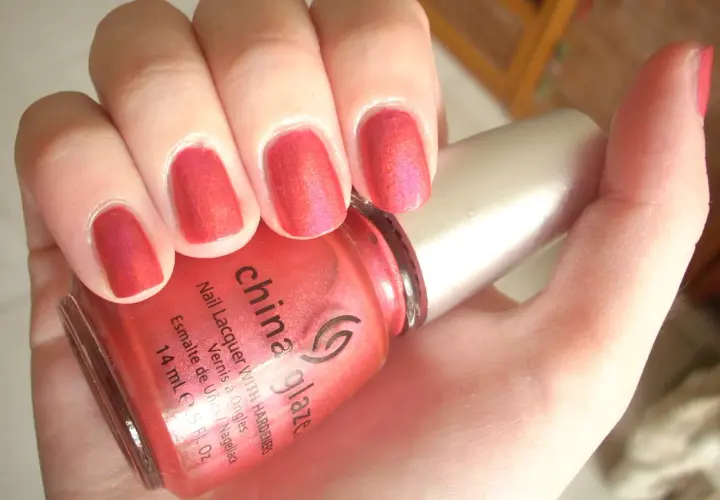 En hand med naglar målade i en glittrig, korallröd nyans. En flaska China Glaze nagellack syns i förgrunden.