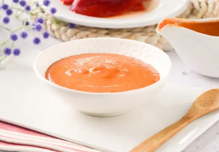 Un cuenco blanco lleno de cremosa salsa de pimientos del piquillo, lista para acompañar tus platos.