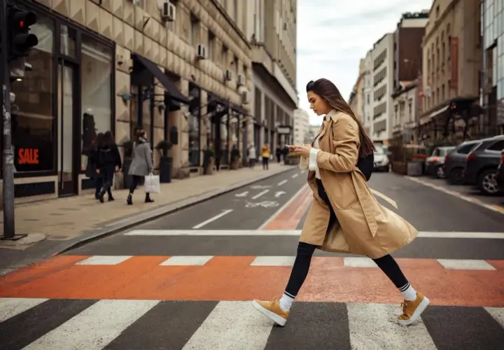 Kobieta w beżowym płaszczu i żółtych sneakersach przechodzi przez pasy. Idealne buty do trencza na miejski spacer.