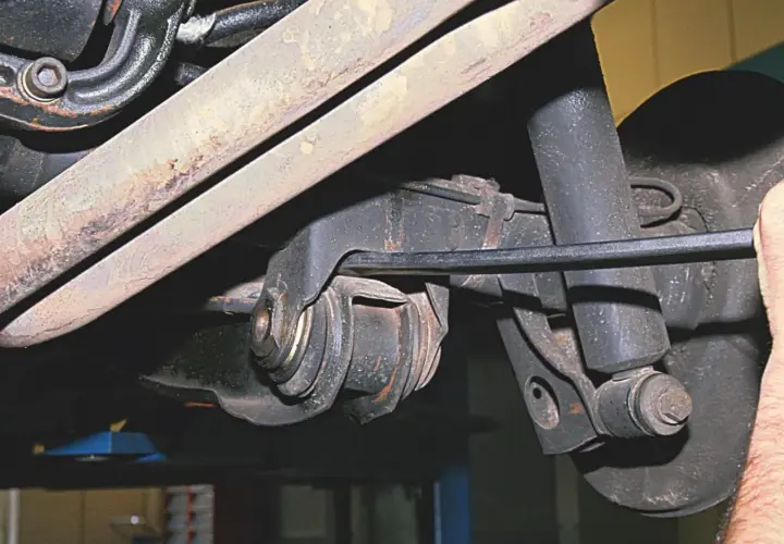 Mechanik pracuje przy wahaczu w samochodzie, używając narzędzia do regulacji.
