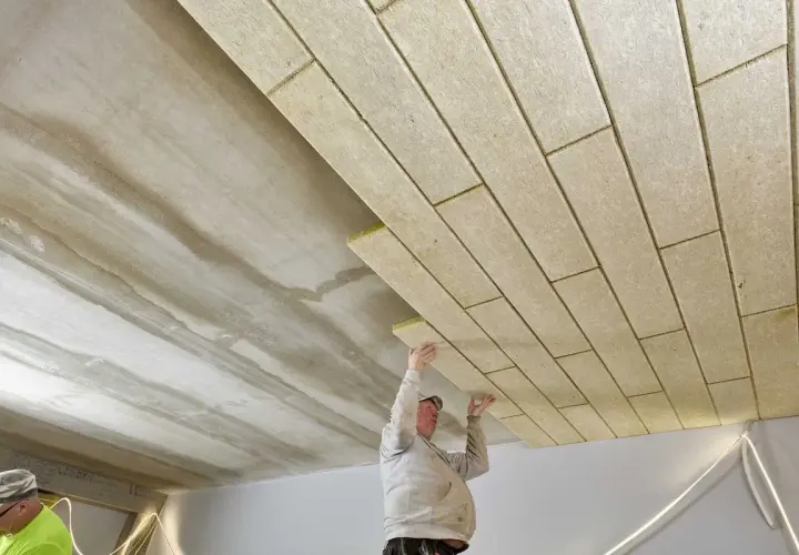 Pracownicy montują płyty izolacyjne, wykonując ocieplenie stropu betonowego.