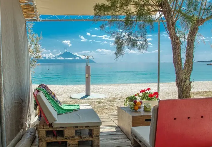 Relaks przy plaży w Armenistis Camping. Leżaki, stolik z owocami i widok na morze z górą w oddali.