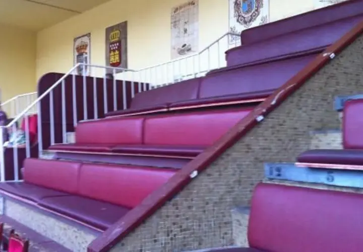 Asientos de terciopelo rojo en un palco de las ventas, con escaleras y barandillas blancas.