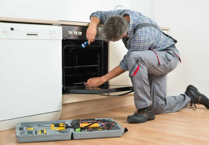 Un technicien effectue le branchement d'un four encastrable, outils à portée de main.