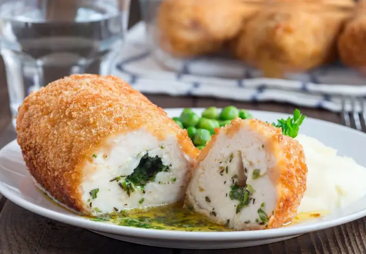 Pyszny kotlet po kijowsku, chrupiący z zewnątrz, soczysty w środku, z zielonym nadzieniem. Podany z puree i groszkiem.