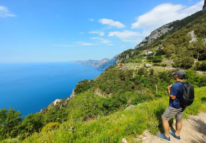 Hiker on a cliff path overlooking the blue sea and coastline.