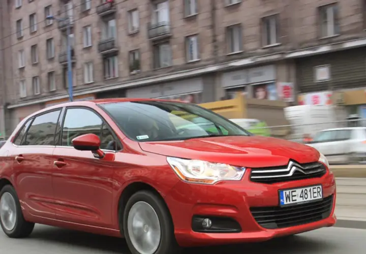 Czerwony Citroen C4 1.6 HDi w ruchu miejskim, z rozmytym tłem budynków i innych pojazdów.