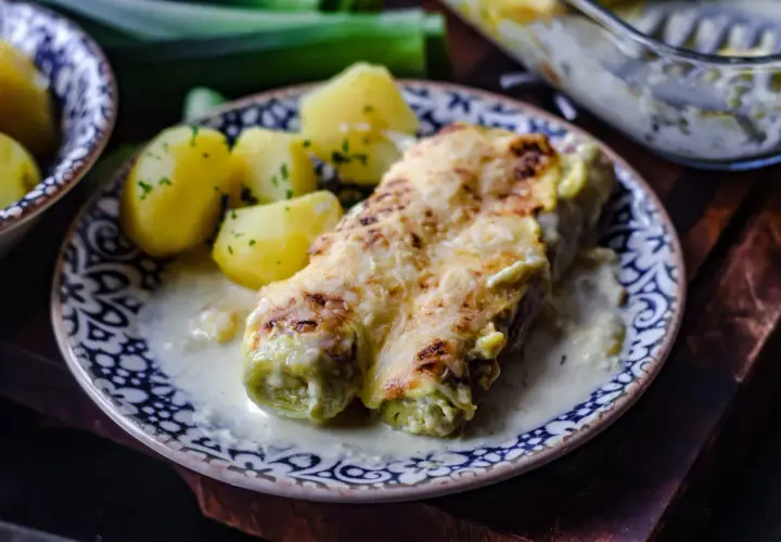 Gebackener Lauch mit Schinken, überbacken mit Käse, serviert mit Salzkartoffeln und einer cremigen Sauce.