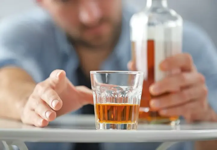 Mężczyzna sięga po szklankę z alkoholem, grozi mu zatrucie alkoholowe.