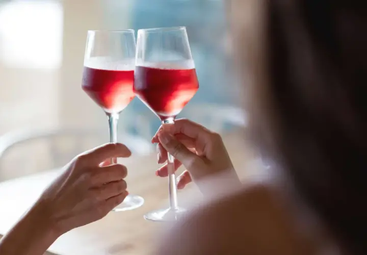 Dwie osoby wznoszą toast kieliszkami z różowym winem. Czy wino różowe powstaje z mieszania białego z czerwonym? Proces produkcji jest ciekawy!