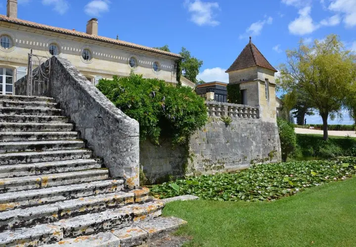 Escalier de pierre menant à un château, avec un étang de nénuphars. Une belle journée pour une visite château Pomerol.
