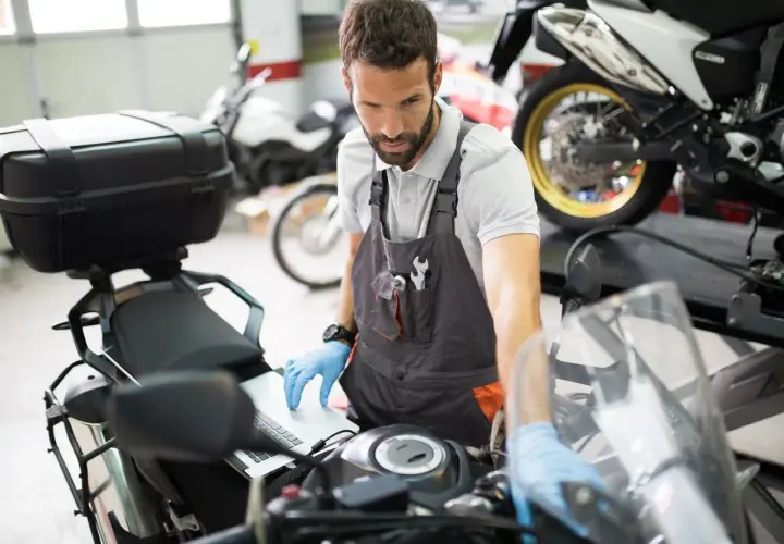 Mecánico revisa en laptop por qué la moto se para en marcha y no arranca.