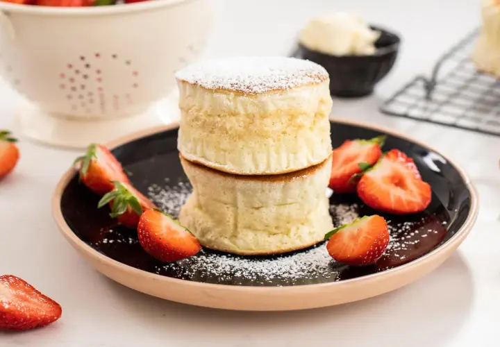 Två fluffiga japanska pannkakor staplade på en tallrik med färska jordgubbar och pudersocker.