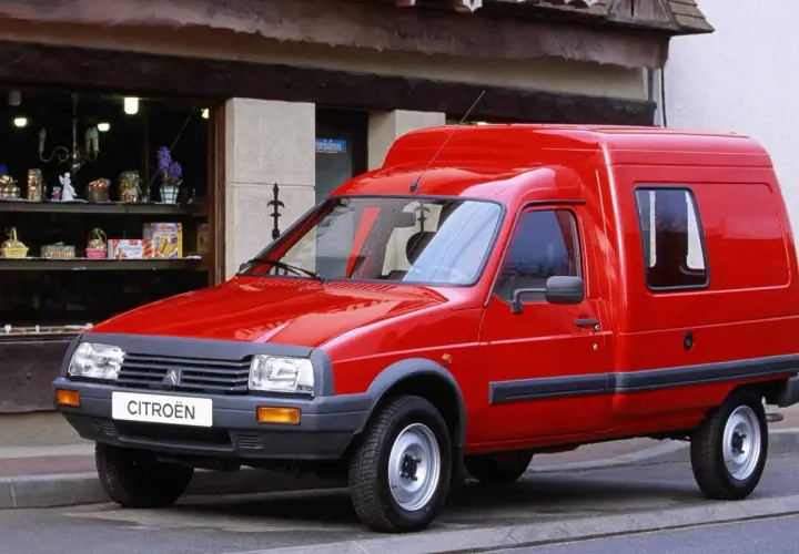 Czerwony van Citroen C15 zaparkowany przed sklepem z witryną pełną drobnych przedmiotów.