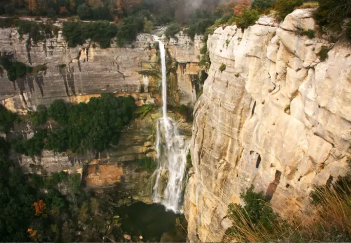 El imponente salt de Sallent cae desde lo alto de acantilados rocosos, rodeado de vegetación exuberante y un paisaje natural impresionante.