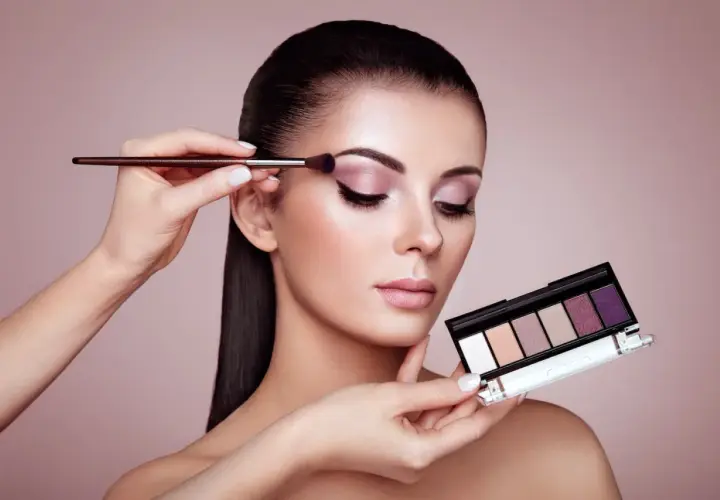 Kobieta zmysłowo maluje powieki, tworząc efekt latte makeup. W dłoni trzyma paletę cieni do powiek.