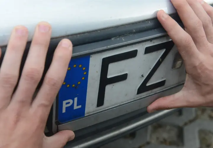 Dłonie trzymają tablicę rejestracyjną z oznaczeniem FZ i symbolem Unii Europejskiej. To ważny etap w procesie bha rejestracja.
