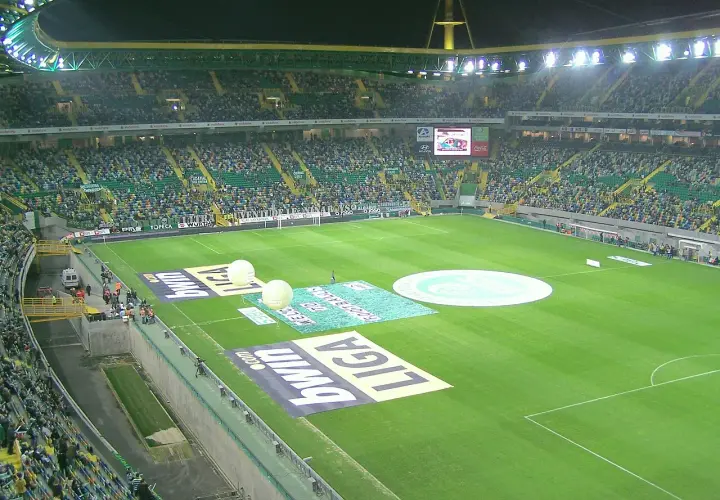 Widok na pełny stadion Sporting Lizbona, z zieloną murawą, trybunami wypełnionymi kibicami i reklamami na boisku.