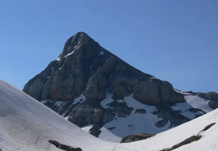 Majestuosa cumbre rocosa en el **valle de Belagua**, con nieve en sus laderas y un cielo azul intenso.