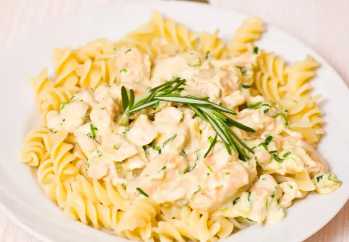 Pyszne tagliatelle z kurczakiem w kremowym sosie, udekorowane gałązką rozmarynu.